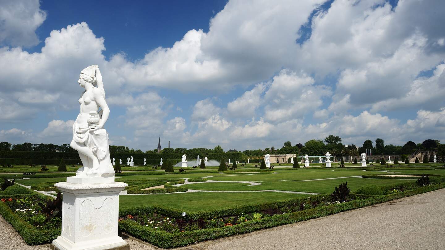 Blick auf die Königlichen Gärten von Herrenhausen in Hannover mit bewölktem Himmel mit einer Statue im Vordergrund | © Gettyimages.com/technotr