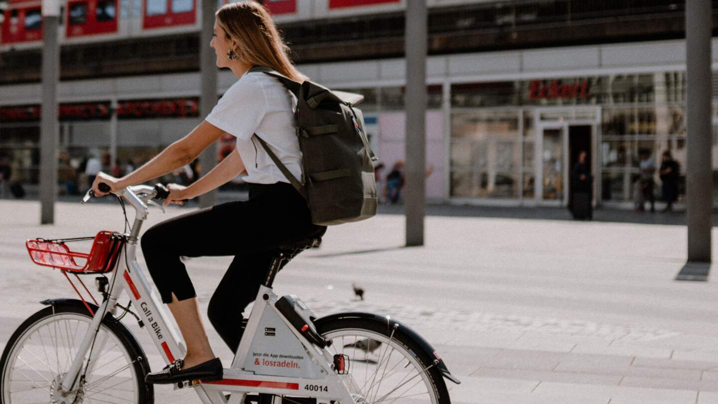 Frau in weißem T-Shirt und mit Rucksack fährt ein Call a Bike in Köln | © Deutsche Bahn AG/Julia Breuer