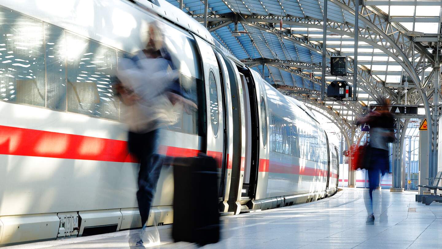 einen modernen Zug an einem Bahnhof, mit einer verschwommenen Figur, die Gepaeck traegt, und einer weiteren Person im Hintergrund | © gettyimages.com/Horst Gerlach