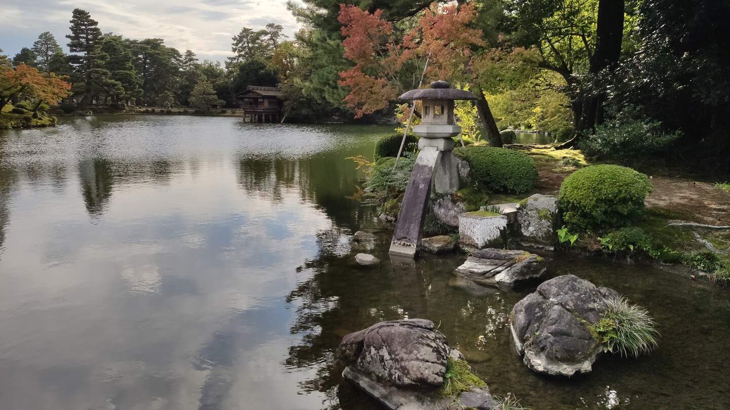 Eine Steinlaterne auf zwei Füßen an einem See im historischen Garten Kenrokuen im Herbst in Kanazawa, Japan | © Jens Hinsche
