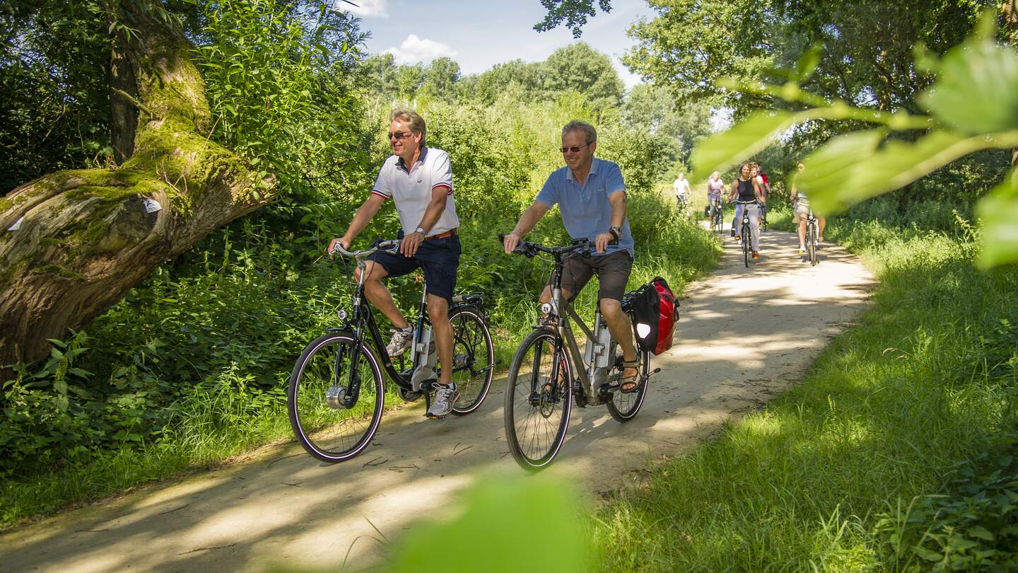 Nahaufname zweier Radfahrer einer Gruppe im Sommer auf einem schmalen, natürlichen Radweg mit viel Grün im Hintergrund im Emsland | © Schoening Fotodesign