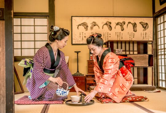 Zwei Frauen in traditionellen Kimonos fuehren eine japanische Teezeremonie in einem klassischen Tatami-Raum durch. | © gettyimages.com/Ababsolutum