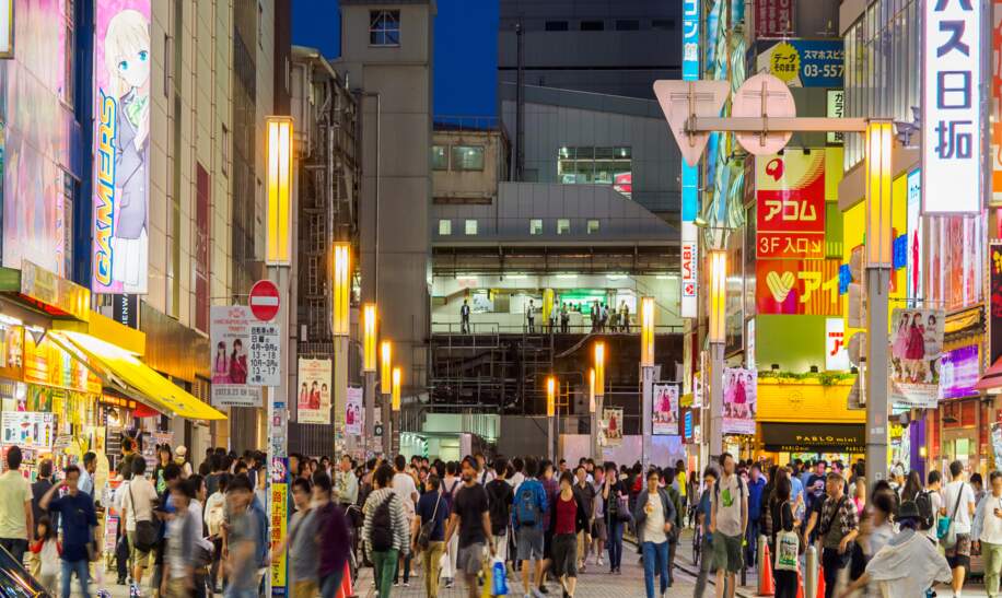 beliebte Strasse in einem Einkaufsviertel bei Nacht, beleuchtet von zahlreichen Leuchtreklamen und gefuellt mit vielen Menschen. | © Gettyimages/kawamura_lucy