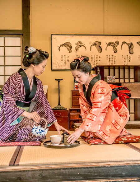 Zwei Frauen in traditionellen Kimonos fuehren eine japanische Teezeremonie in einem klassischen Tatami-Raum durch. | © gettyimages.com/Ababsolutum