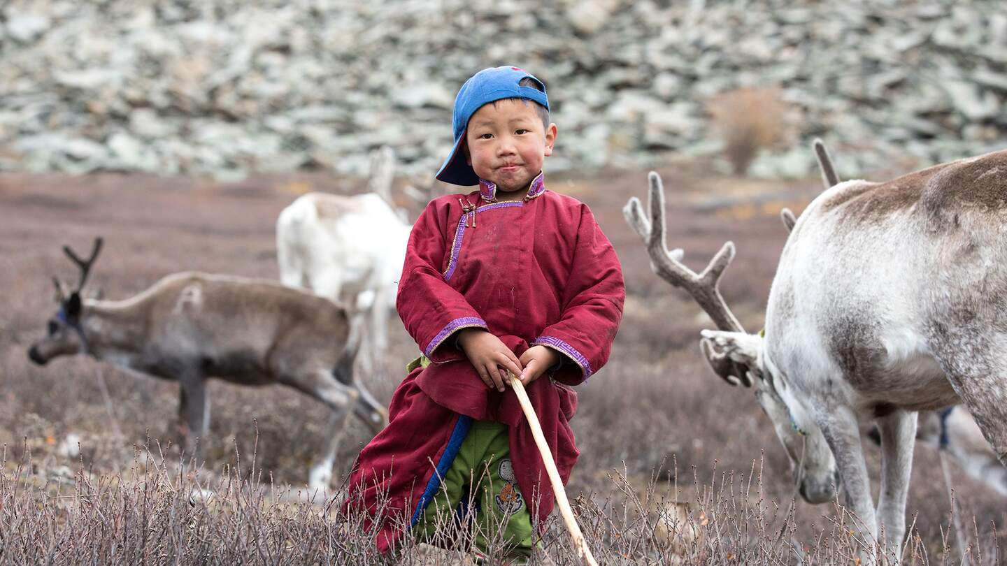 Kleiner tsaatanischer Junge in traditioneller mongolischer Nomadenkleidung posiert mit dem Rentier seiner Familie | © gettyimages.com/kertu_ee