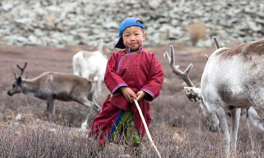 Kleiner tsaatanischer Junge in traditioneller mongolischer Nomadenkleidung posiert mit dem Rentier seiner Familie | © gettyimages.com/kertu_ee