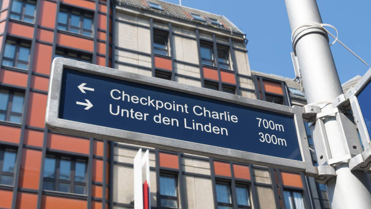 Straßenschild in der berühmten Friedrichstraße in Berlin mit Checkpoint Charlie und weiteren bekannten Sehenswürdigkeiten | © Gettyimages.com/hansenn
