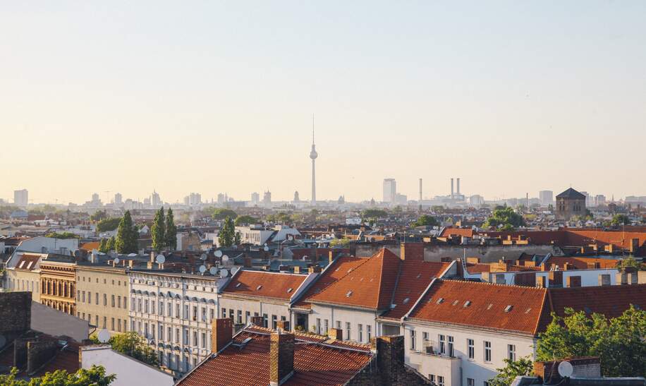 Blick auf das Berliner Panorama vom Dach Neuköllns. Alte Gebäude sowie das Stadtzentrum mit dem berühmten Wahrzeichen des Fernsehturms sind unter dem hellen und klaren Himmel zu sehen. | © Gettyimages.com/lechatnoir