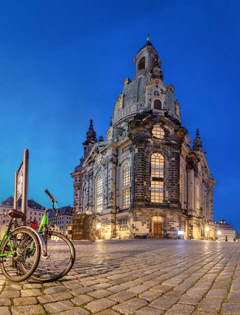 Rückseite der abendlich beleuchteten Frauenkirche Dresden mit Straßencafé und auf gepflastertem Platz geparkten Fahrrädern  | © Gettyimages.com/bbsferrari