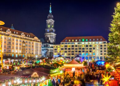 Blick über den Dresdener Weihnachtsmarkt, den Striezelmarkt, mit Weihnachtsbaum und -pyramide, bunt beleuchteten Ständen und der Kreuzkirche im Hintergrund | © Gettyimages.com/Juergen Sack