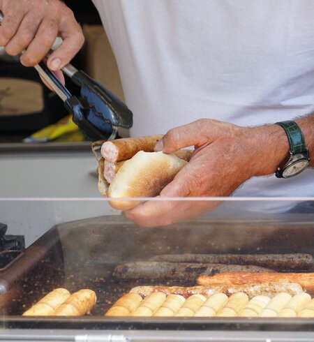 Ein Mann bereitet und eine Grillwurst in einem Brotbrötchen zu. Die "Lange Rote" ist typisch für Freiburg | © Gettyimages.com/Lucia Gajdosikova