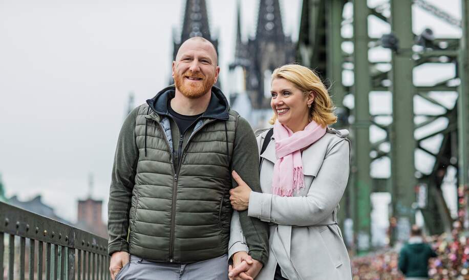 Glückliches Paar, das auf der Hohenzollernbrücke vor dem Dom in Köln steht. | © Gettyimages.com/Lorado