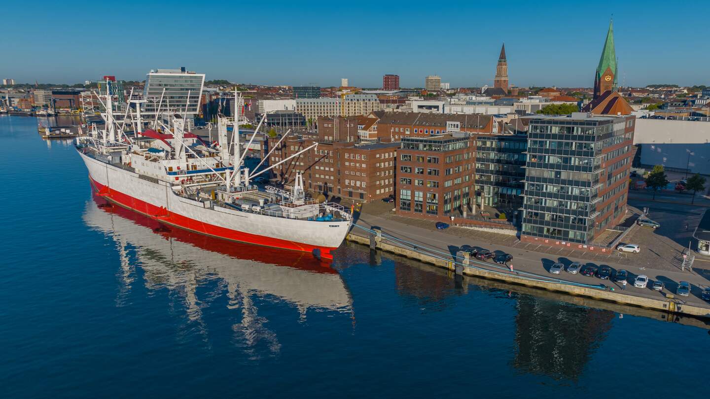 Luftaufnahme des größten Museumsfrachtschiffs der Welt, das im Kieler Hafen vor Anker liegt. Ein weißes und rotes Schiff im Hafen von Kiel. | © Gettyimages.com/frederick doerschem