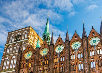 Fassade des historischen Rathauses in Stralsund im Stil der norddeutschen Backsteingotik mit der Nikolaikirche im Hintergrund | © © Gettyimages.com/A-Tom