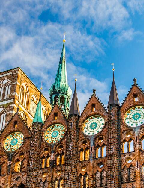 Fassade des historischen Rathauses in Stralsund im Stil der norddeutschen Backsteingotik mit der Nikolaikirche im Hintergrund | © © Gettyimages.com/A-Tom