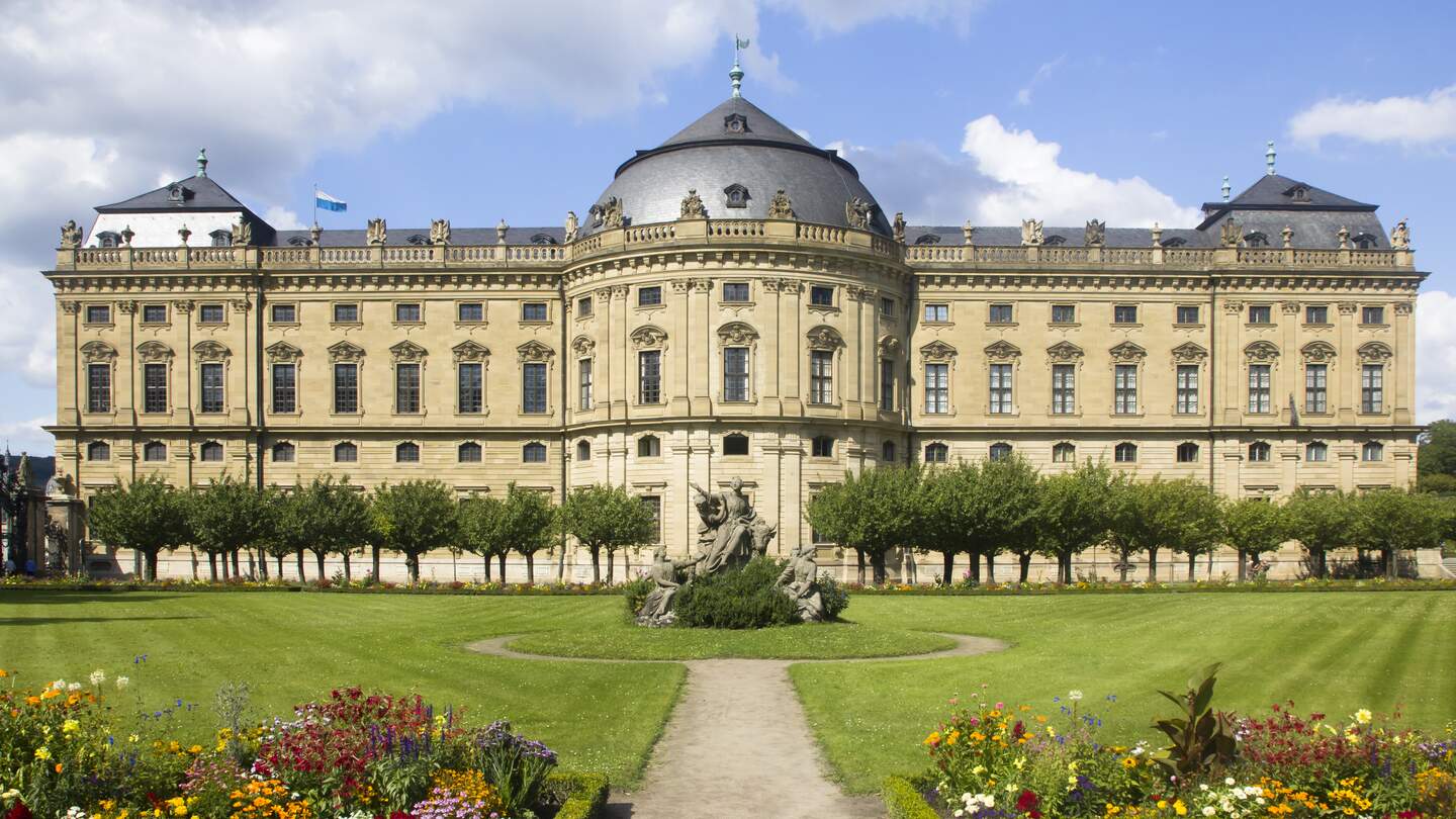 Frontalansicht der Residenz Würzburg mit Blick auf den Felsenbrunnen und blühende Blumen | © Gettyimages.com/Lichtspieler