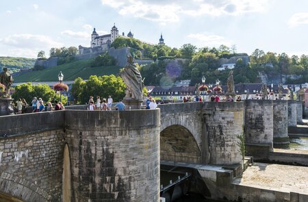 Blick auf die alte Mainbrücke in Würzburg mit Statuen und vielen Toristen bei gutem Wetter | © Gettyimages.com/omersukrugoksu