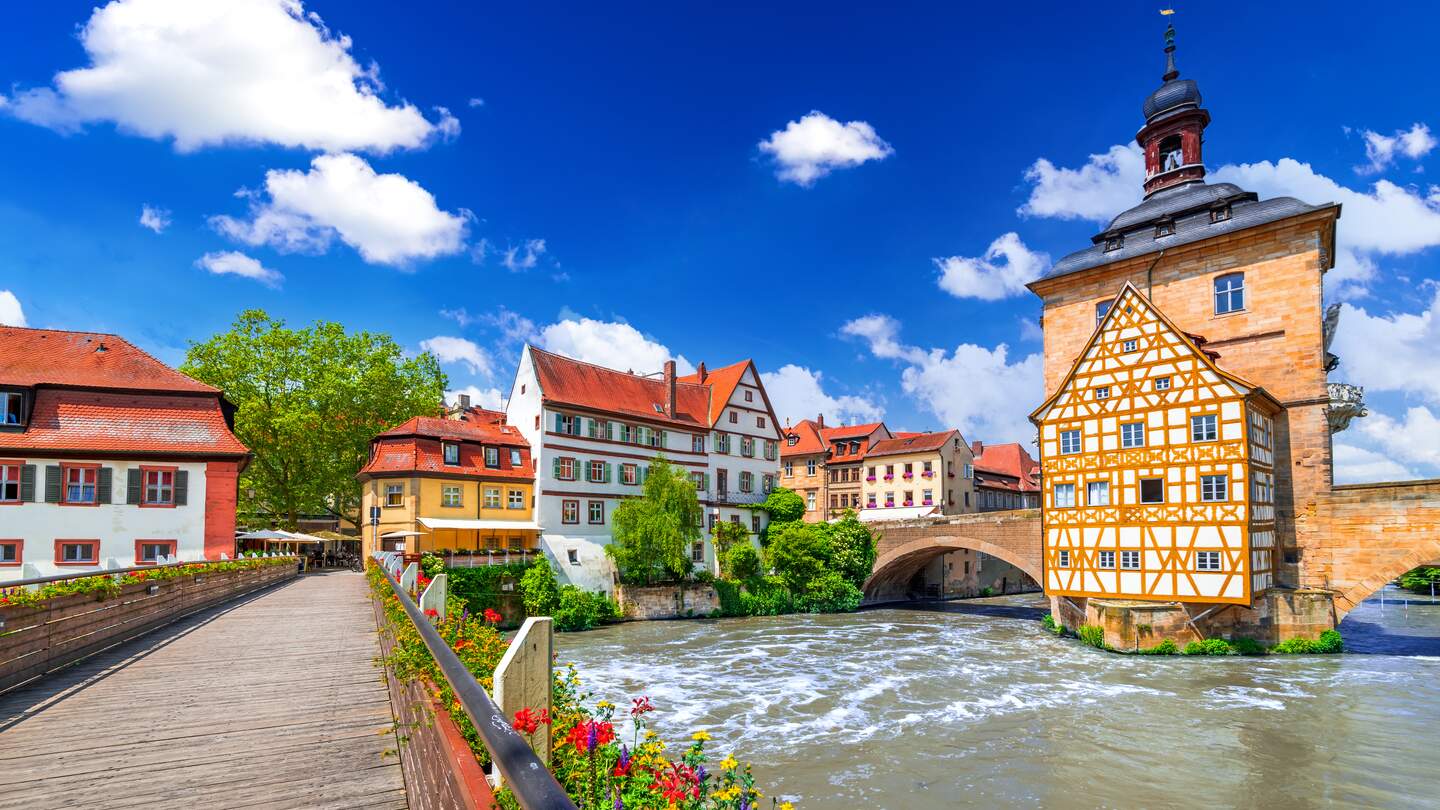 Blick auf das Rathaus und eine mit Blumen geschmueckte Bruecke in Bamberg | © Gettyimages.com/emicristea