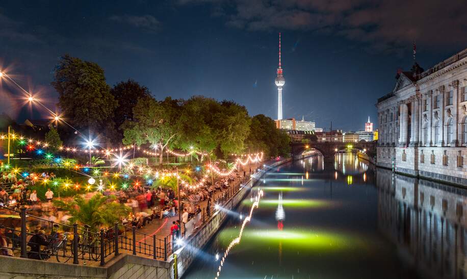 Tanzende Menschen bei Sommer-Strandbar-Beachparty in der Nähe der Spree auf der Museumsinsel mit berühmtem Fernsehturm im Hintergrund bei Nacht, Berlin | © Gettyimages.com/bluejayphoto