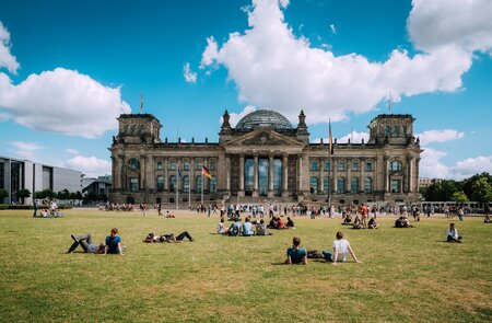 Blick auf das deutsche Parlament in Berlin, genannt Reichstag. Die Menschen ruhen sich aus und liegen auf der Wiese. | © Gettyimages.com/Nikada