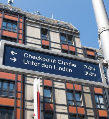 Straßenschild in der berühmten Friedrichstraße in Berlin mit Checkpoint Charlie und weiteren bekannten Sehenswürdigkeiten | © Gettyimages.com/hansenn