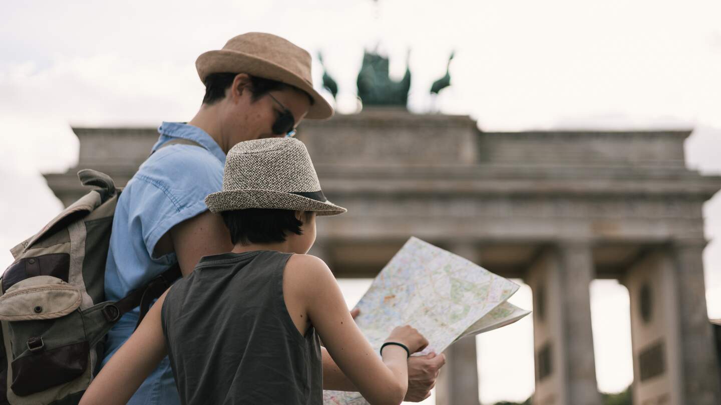 Elternteil mit Kind schaut auf eine Karte am Brandenburger Tor in Berlin | © Gettyimages.com/Amparo Garcia V