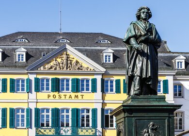 Blick auf Beethoven-Denkmal und Postamt auf dem Muensterplatz in Bonn bei blauem Himmel | © GettyImages.com/worldwidephotoweb