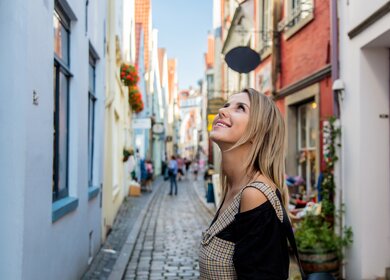 Eine junge Frau spaziert auf einer mittelalterlichen Strasse in Bremen | © Gettyimages.com/Massonstock