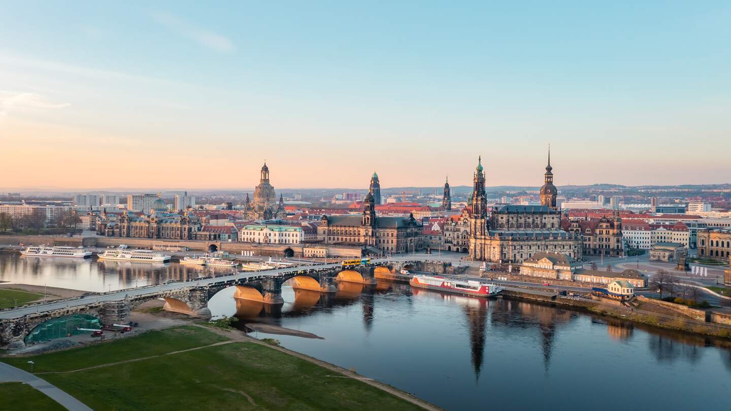 Panoramablick auf die Dresdner Altstadt mit der Elbe und der Augustusbrücke im Vordergrund, historischen Gebäuden wie der Frauenkirche und dem Residenzschloss unter klarem Himmel bei Sonnenuntergang. | © Gettyimages.com/Vladimir Vins