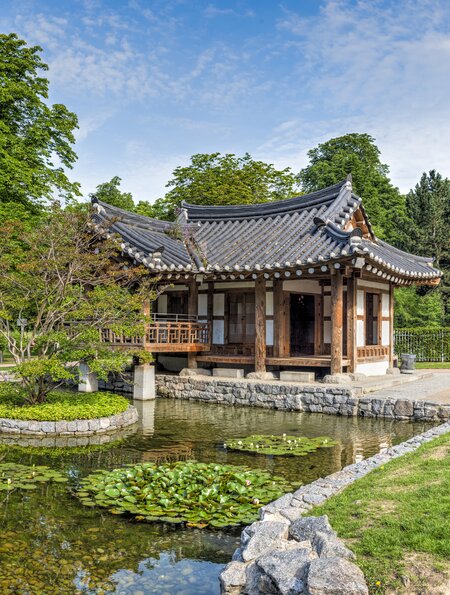 Eine buddhistische Tempelanlage im Grüneburgpark mit typisch asiatischer Architektur bei Sommerwetter und einem Teich im Vordergrund | © Gettyimages.com/Frank Wagner