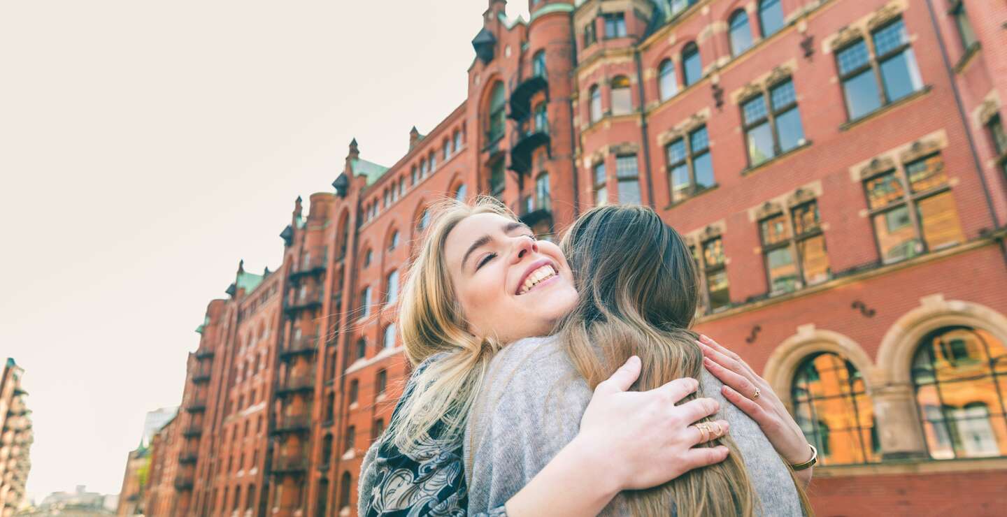 Glueckliche Maedchen, die sich in der Speicherstadt von Hamburg umarmen mit backsteinhäusern im Hintergrund | © Gettyimages.com/william87