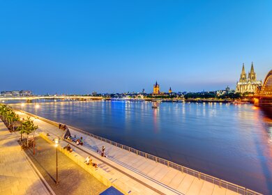 Menschen sitzen am Rheinufer in Köln nach Sonnenuntergang. | © Gettyimages.com/elxeneize