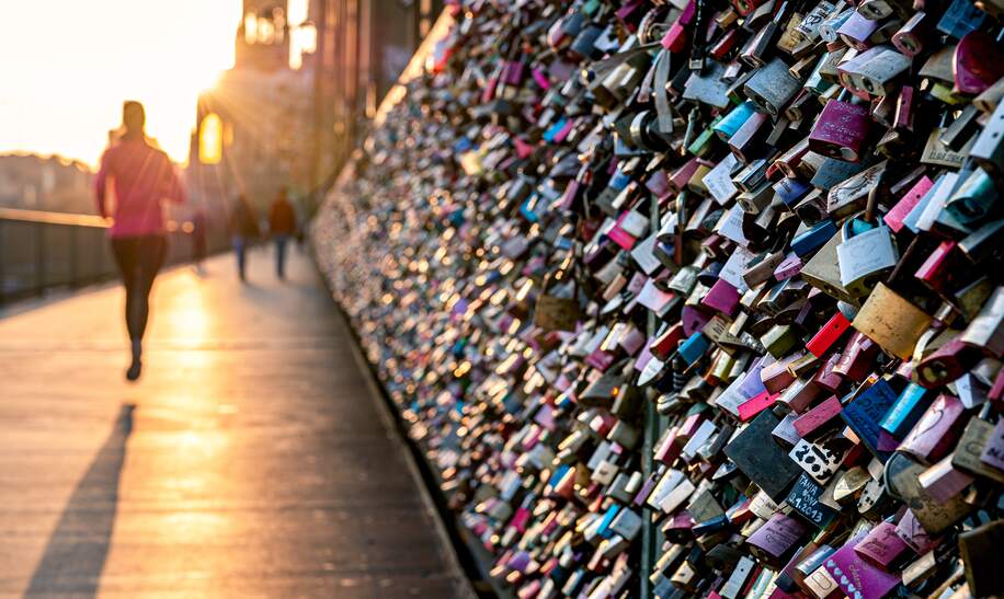 Liebesschlösser am Zaun der Hohenzollernbrücke in Köln im warmen Abendlicht. Menschen, die vorbeikommen. | © Gettyimages.com/Thomas Ramsauer