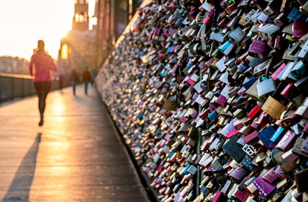 Liebesschlösser am Zaun der Hohenzollernbrücke in Köln im warmen Abendlicht. Menschen, die vorbeikommen. | © Gettyimages.com/Thomas Ramsauer