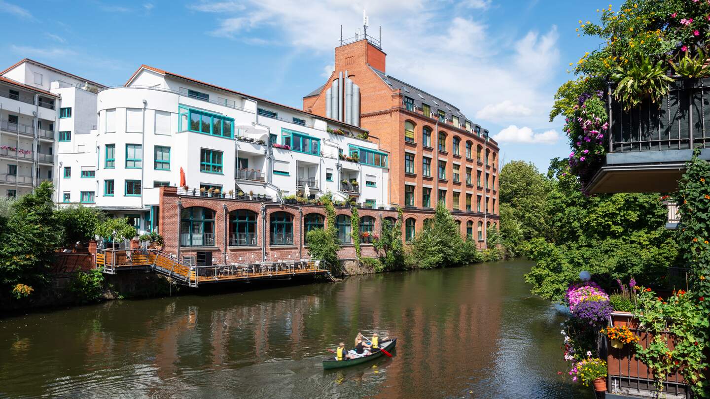 Fluss Elster, auf dem ein Boot fährt, im Szenedistrikt Schleussig mit schönen Loft in alten Industriegebäuden in Leipzig | © Gettyimages.com/kamisoka