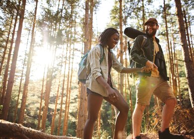 Glueckliches Paar, die in einem Wald wandern, wobei eine Person der anderen hilft.  | © Gettyimages.com/eclipse_images