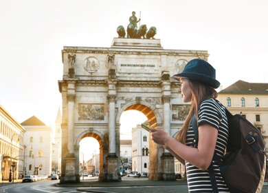 Eine Frau mit einem Rucksack betrachtet den Trimphbogen in München  | © Gettyimages.com/franz12