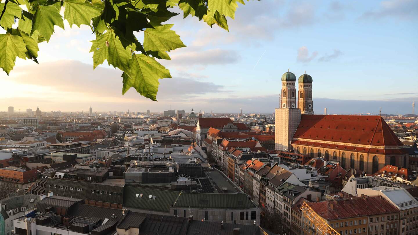 Skyline von Muenchen mit Frauenkirche im Fokus und Blättern am oberen Rand des Bildes | © Gettyimages.com/alexsl