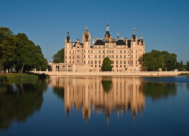  Schloss mit vielen Tuermen und Verzierungen, das sich malerisch im ruhigen Wasser spiegelt. | © gettyImages.com/RicoK69