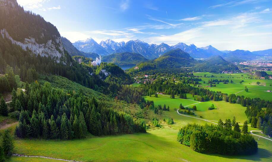 Schloss Neuschwanstein in der Ferne, liegt auf einem schroffen Huegel ueber dem Dorf Hohenschwangau im suedwestlichen Bayern | © Gettyimages.com/MNStudio