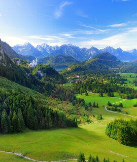 Beruehmtes Schloss Neuschwanstein sehen in der Ferne, liegt auf einem schroffen Huegel über dem Dorf Hohenschwangau im suedwestlichen Bayern | © Gettyimages.com/MNStudio
