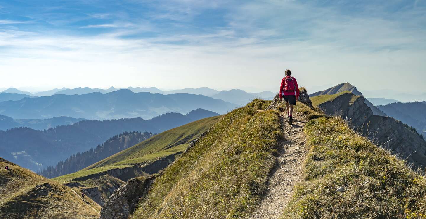 Eine aeltere Frau wandert im Herbst auf dem Grat der Nagelfluhkette bei Oberstaufen im Allgaeu, Bayern, Deutschland, mit dem Hochgrats-Gipfel im Hintergrund. | © Gettyimages.com/Uwe Moser