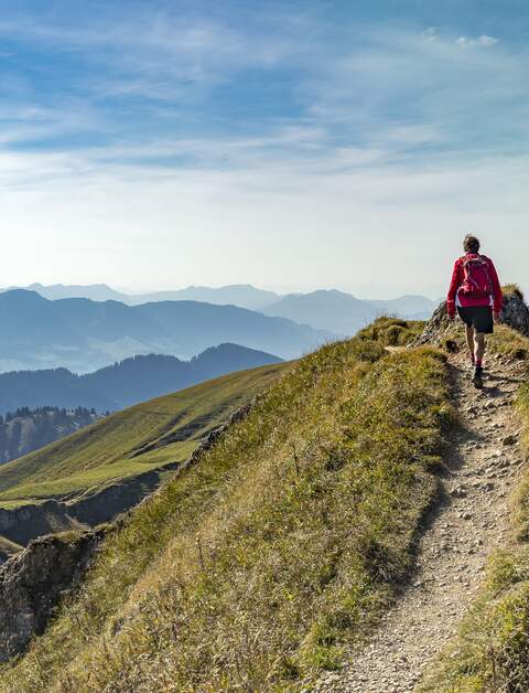 Eine aeltere Frau wandert im Herbst auf dem Grat der Nagelfluhkette bei Oberstaufen im Allgaeu, Bayern, Deutschland, mit dem Hochgrats-Gipfel im Hintergrund. | © Gettyimages.com/Uwe Moser