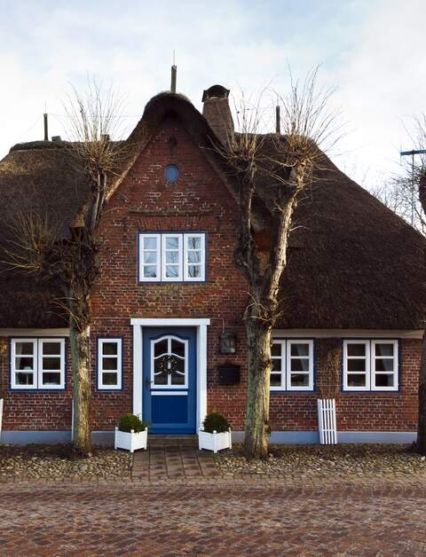 Friesisches Reetdachhaus hinter einer gepflasterten Straße in Nieblum auf Föhr, Schleswig-Holstein | © © Gettyimages.com/eyewave