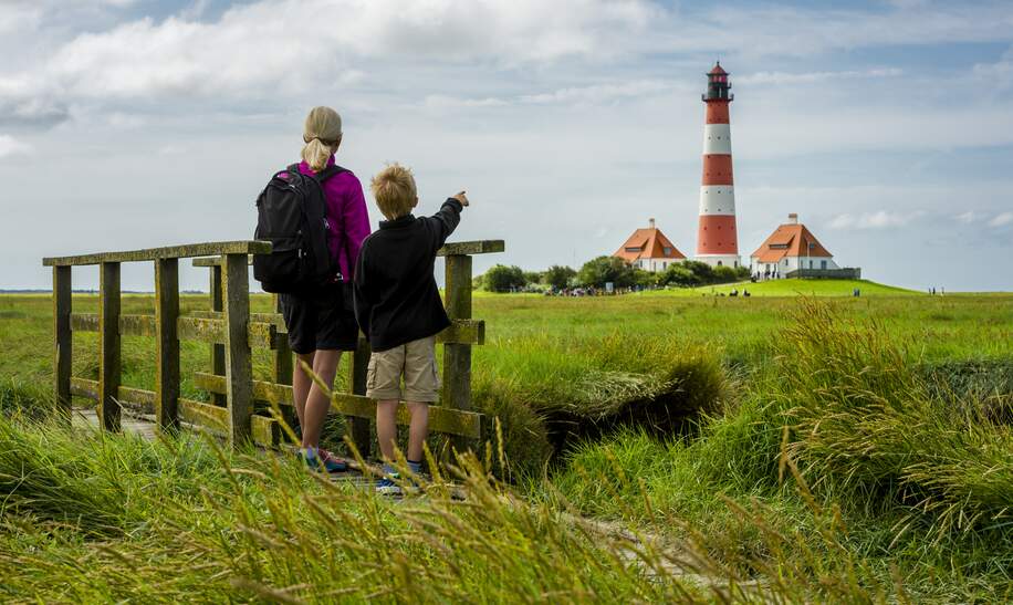 Frau und Junge stehen auf einer kleinen Bruecke und schauen in Richtung des Leuchturms von Westhever | © Gettyimages.com/no_limit_pictures