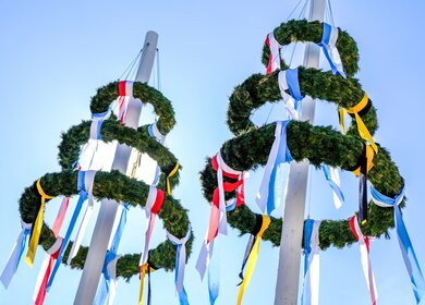Typischer Bayrischer Maibaum mit Kraenzen und bunten Baendern | © Gettyimages.com/FooTToo