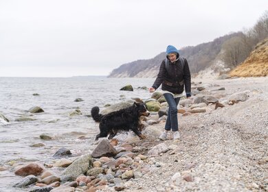 Die reife Frau geht im Winter mit ihrem belgischen Zennenhund an der felsigen und sandigen Kueste der Ostsee spazieren. | © Gettyimages.com/potemkin