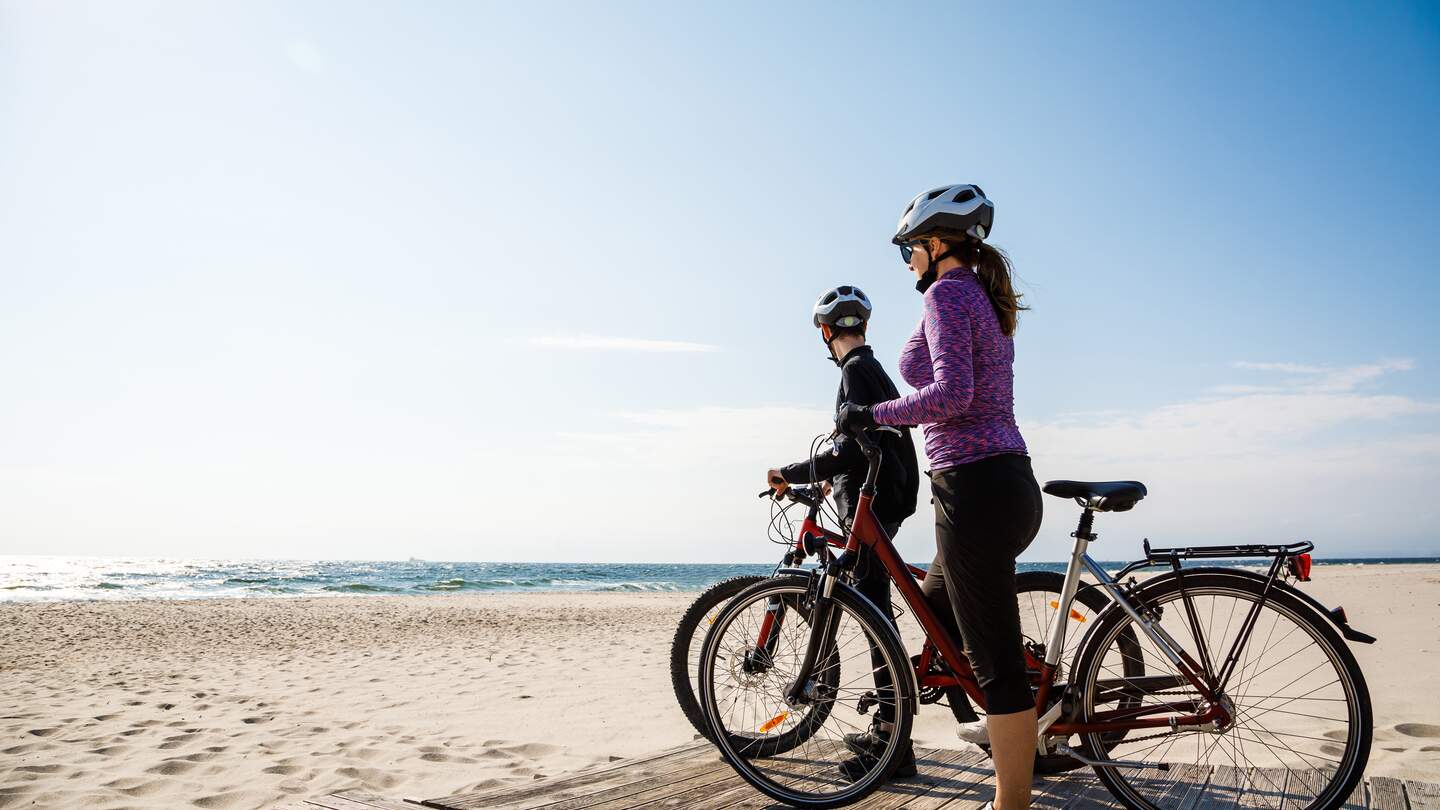 Paar mit Fahrraedern am Strand mit Blicken auf das Meer mit strahlend blauem Himmel | © Gettyimage/gbh007