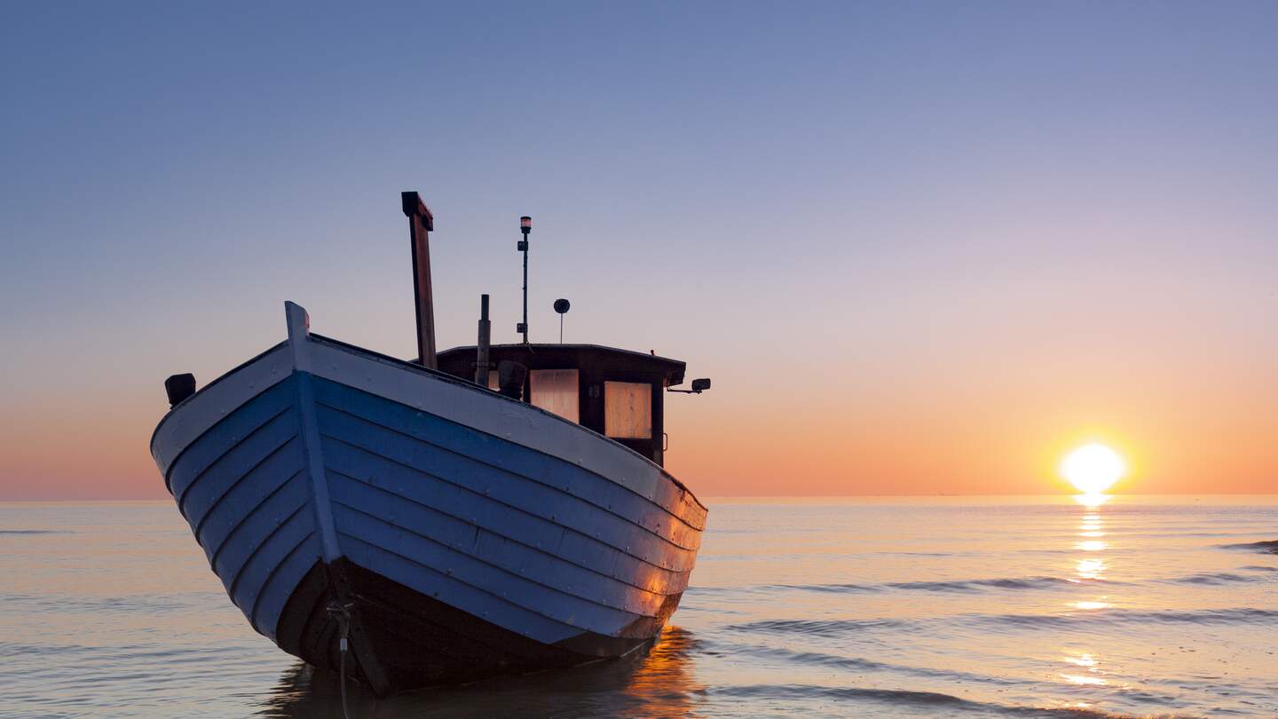 Typisches Fischerboot an der Ostsee im Sonnenuntergang am Strand | © gettyimages.com/nicky39