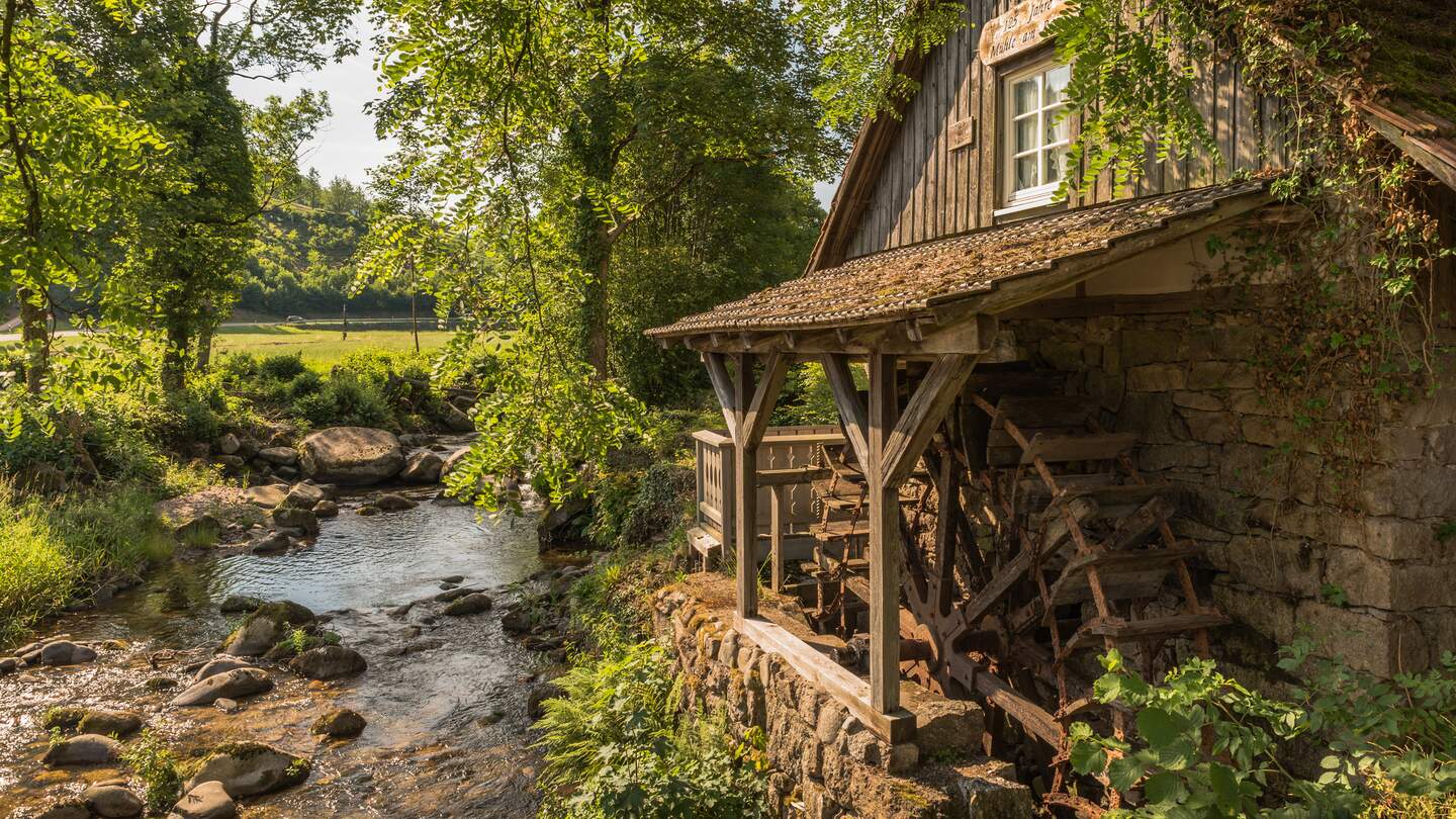 Traditionelle Wassermühle entlang eines Baches, umgeben von Bäumen und Wiesen. Die berühmte Rainbauernmühle bei Ottenhöfen, Baden-Württemberg, Deutschland | © Gettyimages.com/connypokorny